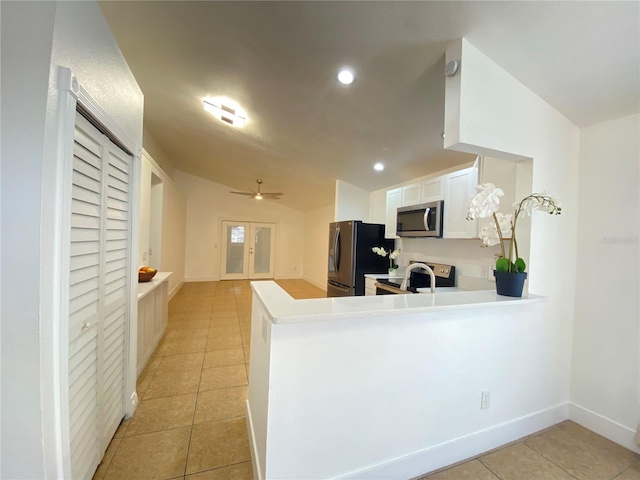 kitchen featuring lofted ceiling, kitchen peninsula, light tile patterned floors, appliances with stainless steel finishes, and white cabinetry