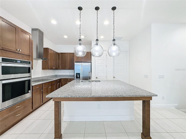 kitchen featuring hanging light fixtures, wall chimney range hood, a kitchen island with sink, a breakfast bar, and appliances with stainless steel finishes