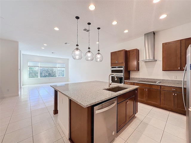 kitchen featuring hanging light fixtures, stainless steel appliances, wall chimney range hood, an island with sink, and light tile patterned floors