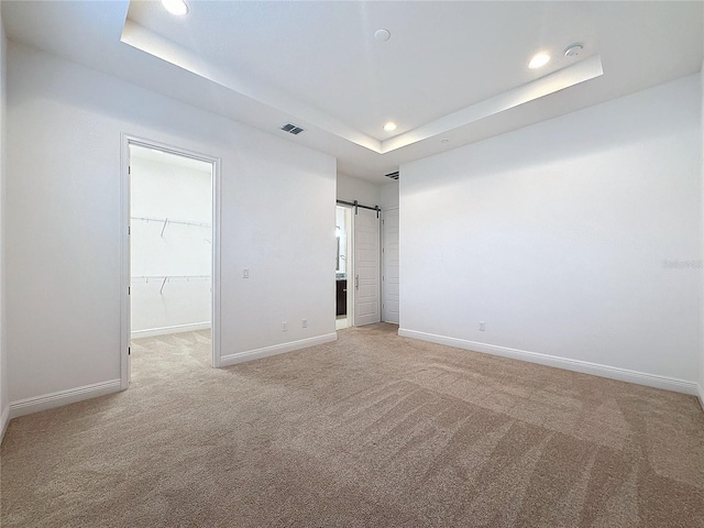 carpeted spare room featuring a barn door and a tray ceiling