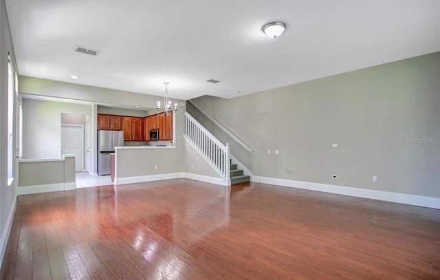 unfurnished living room featuring an inviting chandelier and light wood-type flooring