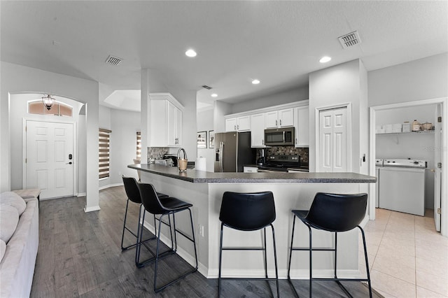 kitchen featuring white cabinets, light hardwood / wood-style floors, kitchen peninsula, stainless steel appliances, and washer / clothes dryer