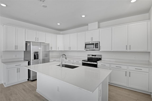 kitchen featuring sink, appliances with stainless steel finishes, a kitchen island with sink, white cabinets, and light wood-type flooring