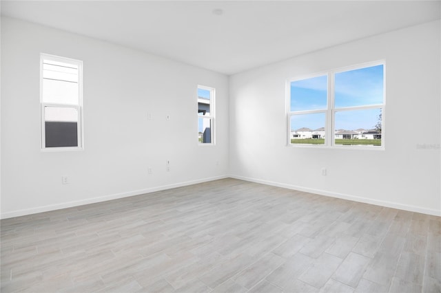 spare room with light wood-style floors, a wealth of natural light, and baseboards