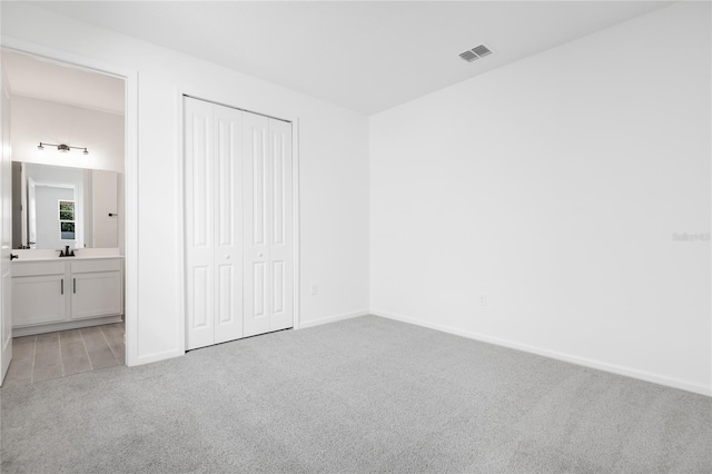 unfurnished bedroom with a closet, visible vents, light carpet, and baseboards