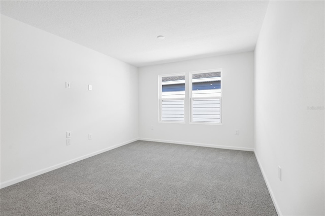 carpeted spare room featuring a textured ceiling and baseboards