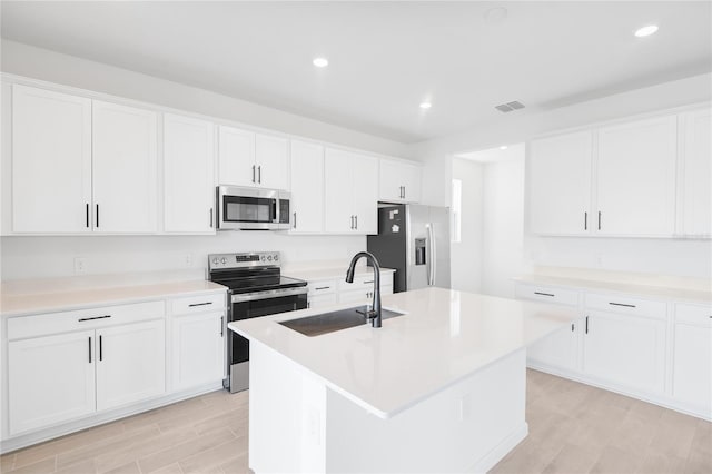 kitchen with visible vents, appliances with stainless steel finishes, a kitchen island with sink, a sink, and white cabinetry