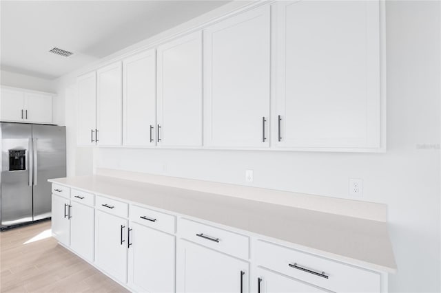 kitchen featuring light wood finished floors, light countertops, visible vents, white cabinetry, and stainless steel fridge with ice dispenser