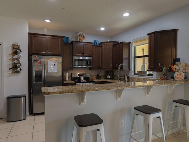 kitchen with a breakfast bar, light stone countertops, stainless steel appliances, and kitchen peninsula