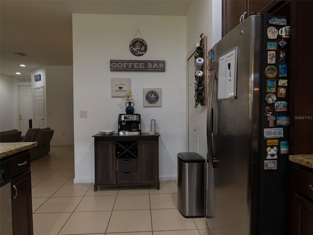 kitchen with light tile patterned floors, dark brown cabinetry, stainless steel refrigerator, and light stone counters