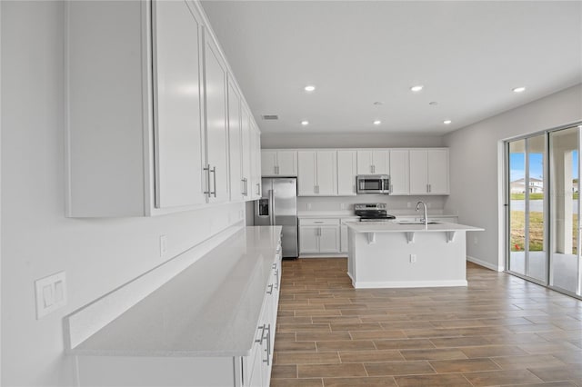 kitchen featuring an island with sink, sink, white cabinets, a kitchen bar, and stainless steel appliances