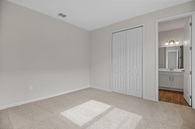 unfurnished bedroom featuring ensuite bathroom, sink, dark carpet, and a closet