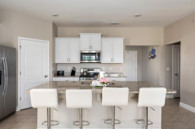 kitchen featuring a kitchen bar, stainless steel appliances, white cabinetry, and an island with sink