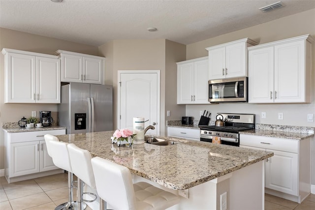 kitchen with a textured ceiling, white cabinetry, a kitchen island with sink, and appliances with stainless steel finishes