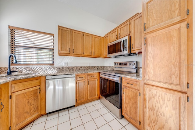 kitchen with stainless steel appliances, a sink, light stone counters, and light tile patterned floors