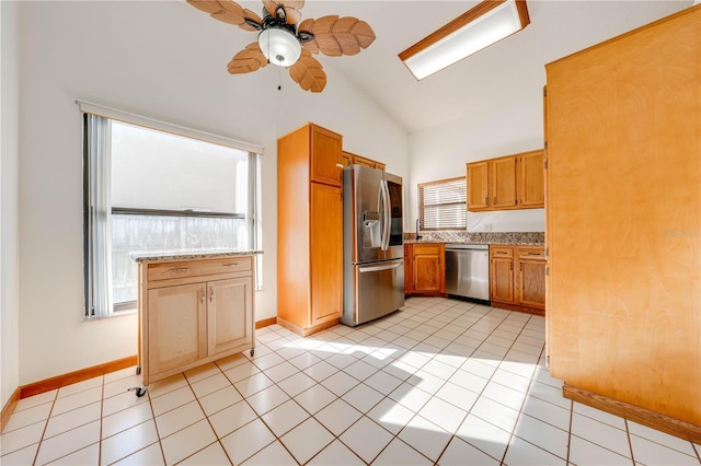 kitchen featuring light stone counters, stainless steel appliances, ceiling fan, light tile patterned floors, and high vaulted ceiling