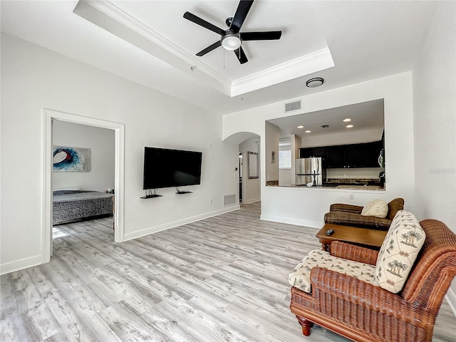 living room with light wood-type flooring, a tray ceiling, ceiling fan, and ornamental molding