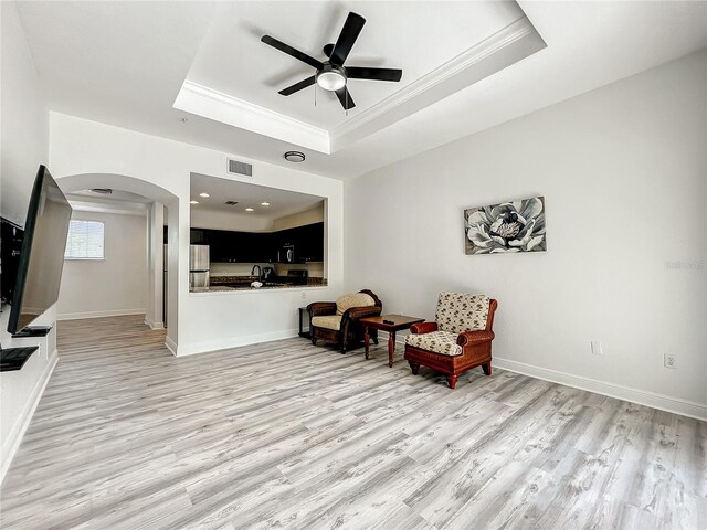 living area featuring a tray ceiling, crown molding, ceiling fan, and light hardwood / wood-style floors