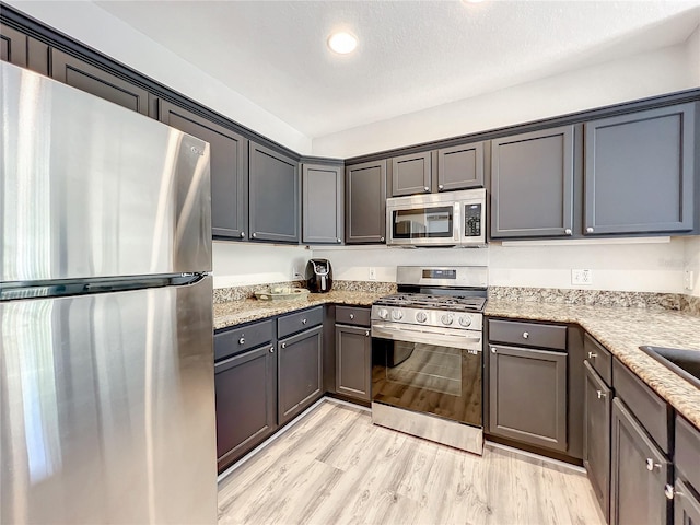 kitchen featuring a textured ceiling, appliances with stainless steel finishes, light wood-type flooring, and light stone counters