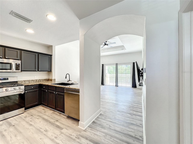 kitchen featuring arched walkways, stainless steel appliances, a sink, visible vents, and light wood-type flooring