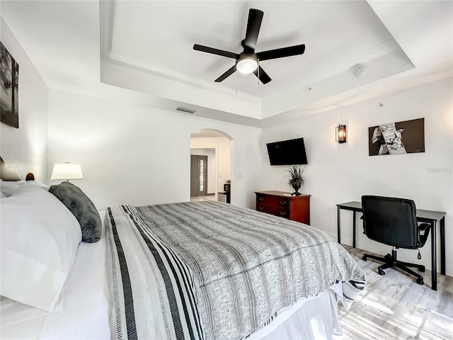 bedroom with a tray ceiling, ceiling fan, and light wood-type flooring