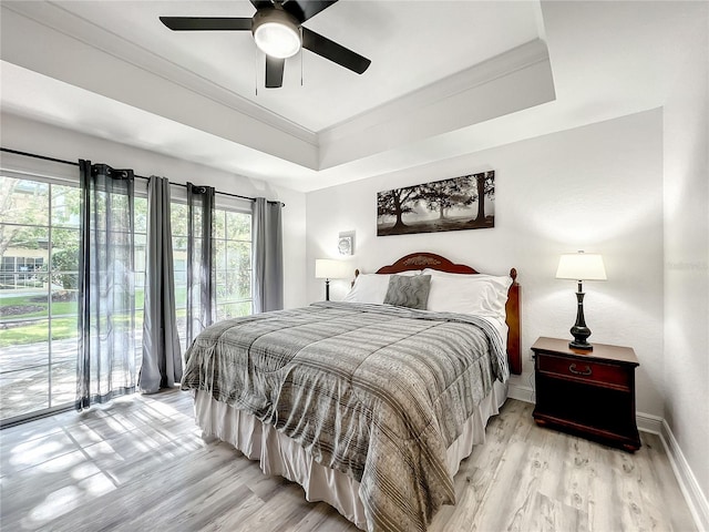 bedroom featuring access to exterior, light wood-style flooring, baseboards, and a raised ceiling