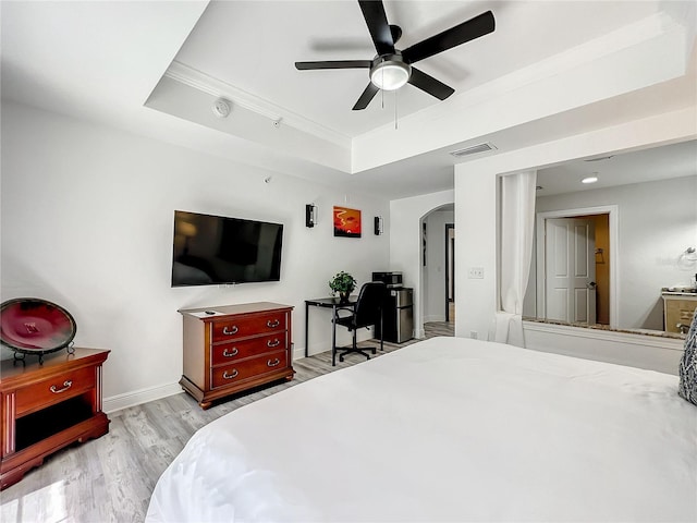 bedroom with arched walkways, a raised ceiling, visible vents, wood finished floors, and baseboards