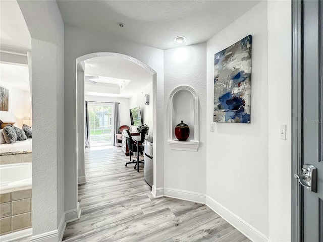 hall with arched walkways, baseboards, a textured wall, and light wood finished floors