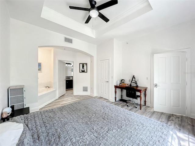 bedroom featuring light hardwood / wood-style flooring, a raised ceiling, ceiling fan, and ensuite bathroom