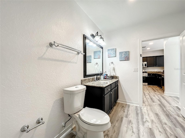 bathroom featuring baseboards, a textured wall, toilet, wood finished floors, and vanity