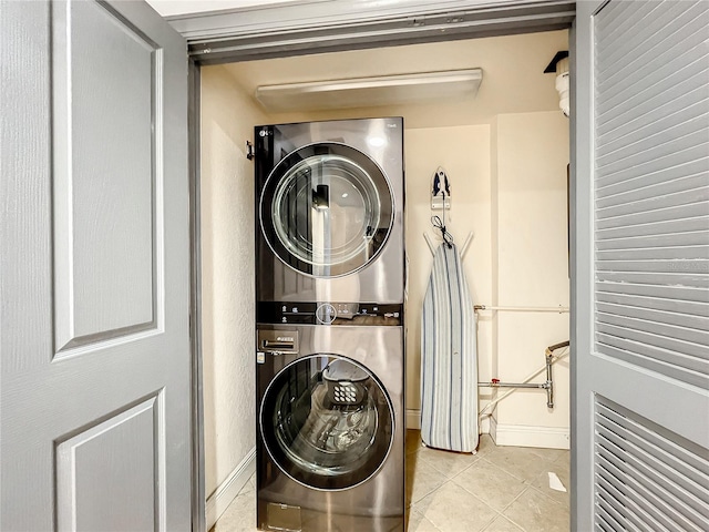 clothes washing area featuring laundry area, stacked washing maching and dryer, light tile patterned flooring, and baseboards