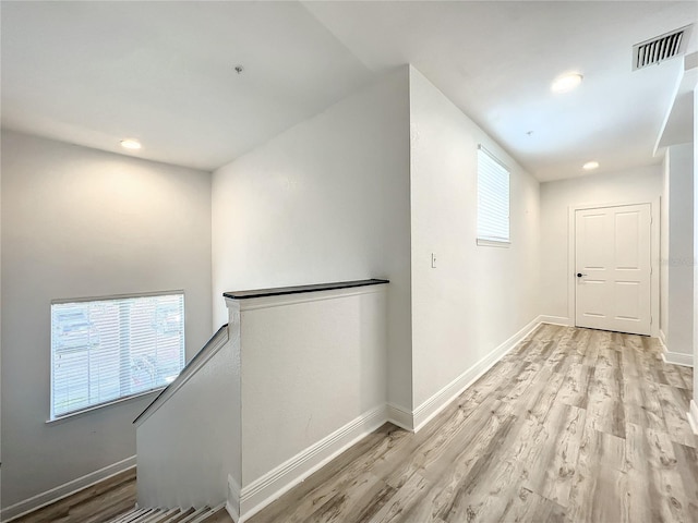 hall featuring baseboards, visible vents, light wood-style flooring, and an upstairs landing