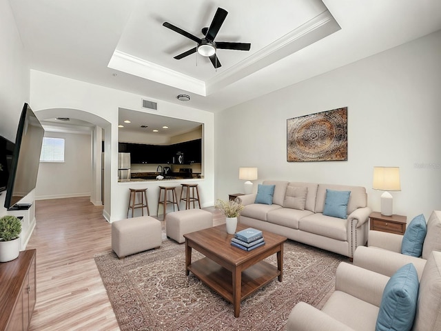 living area with a ceiling fan, light wood-type flooring, a raised ceiling, and arched walkways