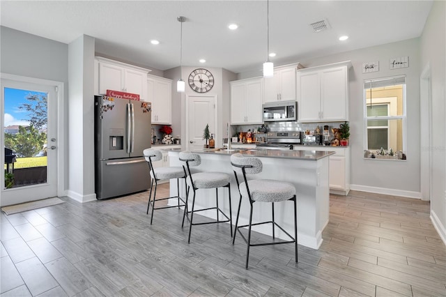 kitchen featuring stainless steel appliances, pendant lighting, light hardwood / wood-style flooring, white cabinetry, and an island with sink