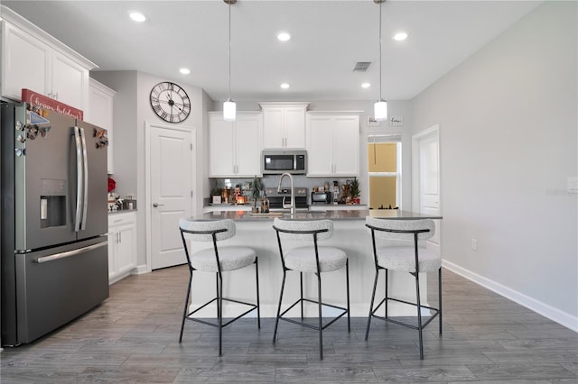 kitchen with white cabinets, pendant lighting, an island with sink, and stainless steel appliances