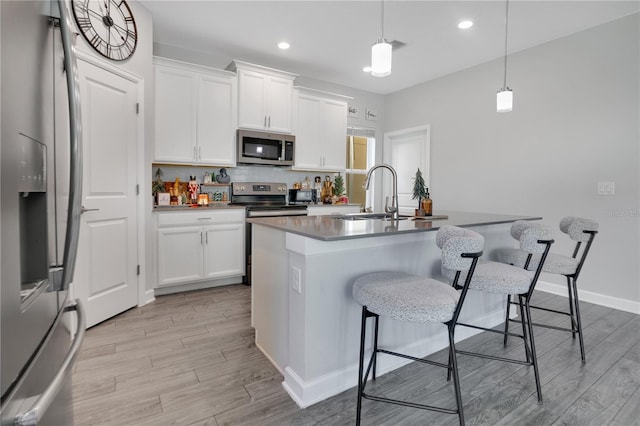 kitchen featuring white cabinets, a kitchen island with sink, hanging light fixtures, and appliances with stainless steel finishes