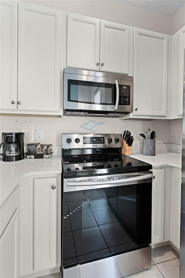 kitchen with light tile patterned flooring, white cabinets, and stainless steel appliances