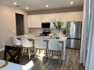 kitchen with white cabinets, an island with sink, appliances with stainless steel finishes, and dark wood-type flooring