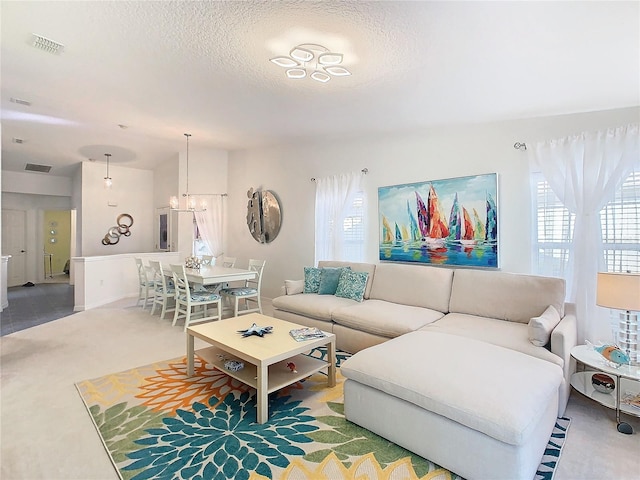 carpeted living room with plenty of natural light, a textured ceiling, and an inviting chandelier