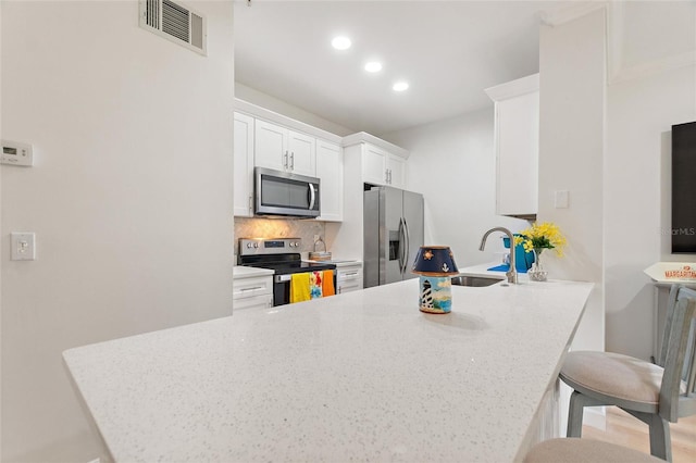 kitchen with sink, kitchen peninsula, a breakfast bar area, white cabinetry, and stainless steel appliances