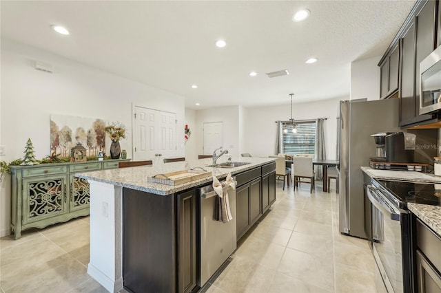 kitchen with appliances with stainless steel finishes, dark brown cabinets, a kitchen island with sink, sink, and pendant lighting