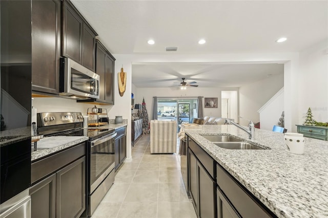 kitchen featuring light stone countertops, appliances with stainless steel finishes, dark brown cabinetry, ceiling fan, and sink