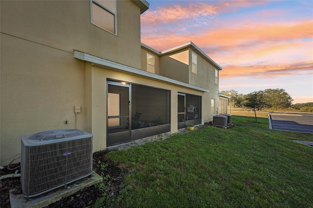 back house at dusk featuring a lawn and central AC