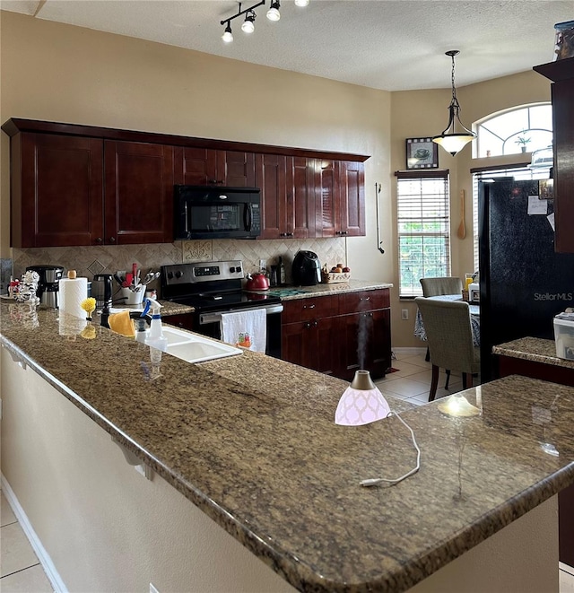 kitchen with kitchen peninsula, dark stone countertops, light tile patterned flooring, and black appliances