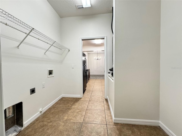 clothes washing area with washer hookup, a textured ceiling, electric dryer hookup, and light tile patterned flooring