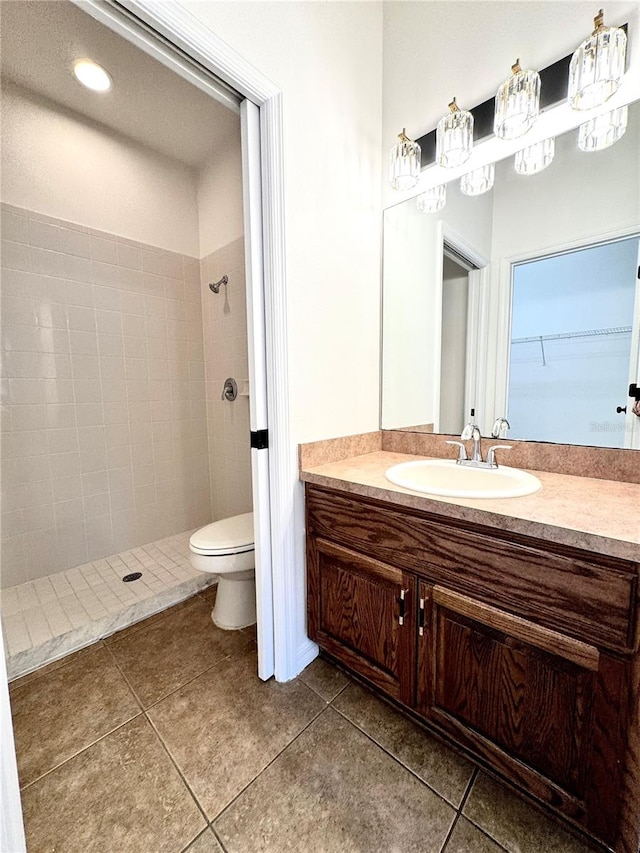 bathroom with tile patterned flooring, toilet, a tile shower, and vanity