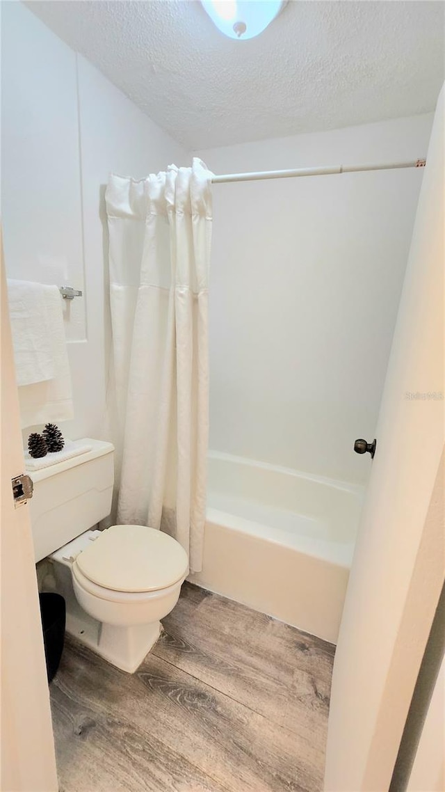 bathroom featuring a textured ceiling, hardwood / wood-style flooring, toilet, and shower / bath combo with shower curtain