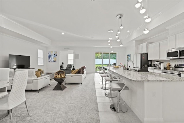 kitchen with white cabinets, hanging light fixtures, an island with sink, appliances with stainless steel finishes, and light stone counters