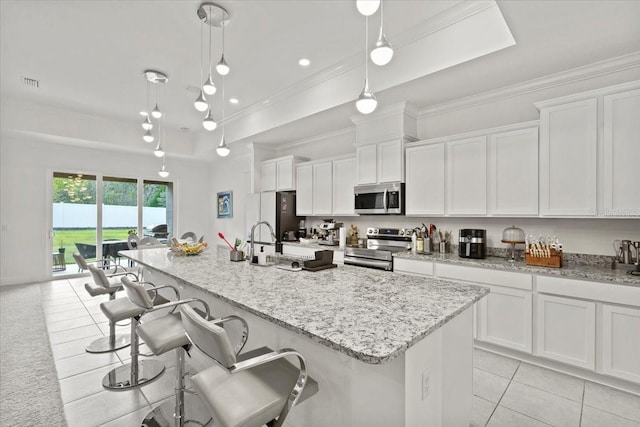 kitchen with appliances with stainless steel finishes, a center island with sink, white cabinetry, and pendant lighting