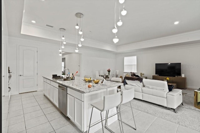 kitchen with hanging light fixtures, light stone counters, stainless steel dishwasher, a kitchen island with sink, and white cabinets